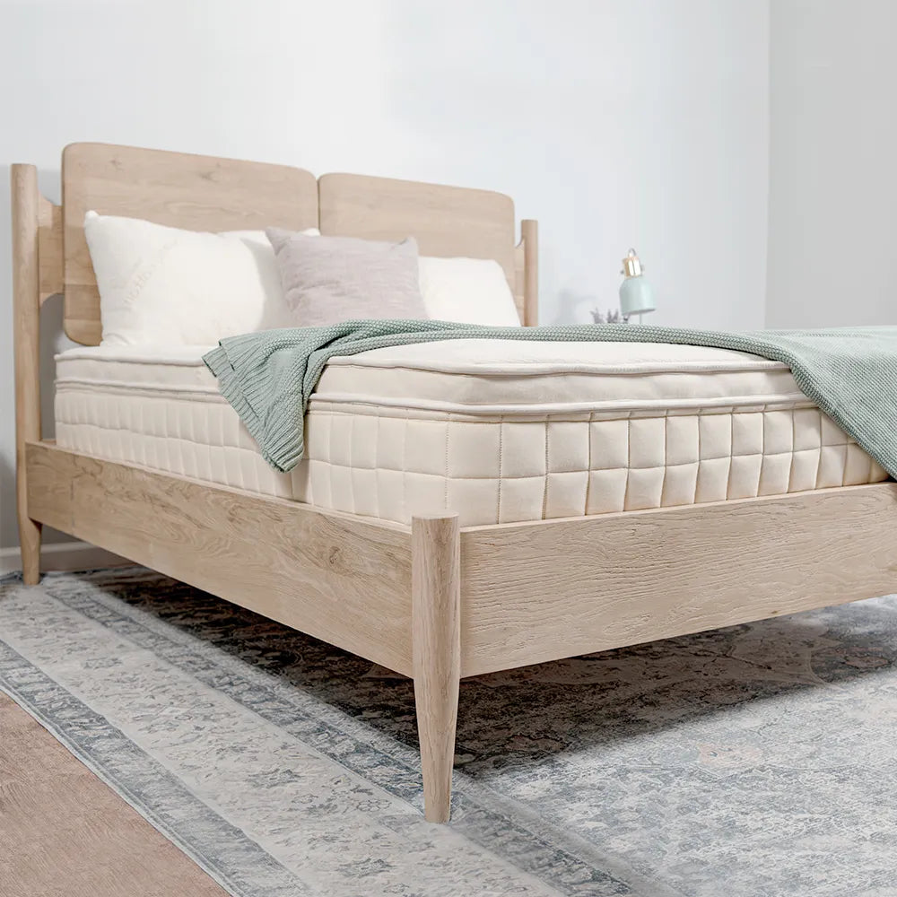 Naturepedic organic mattress on a light wood bed frame, styled with white and gray pillows, a sage green blanket