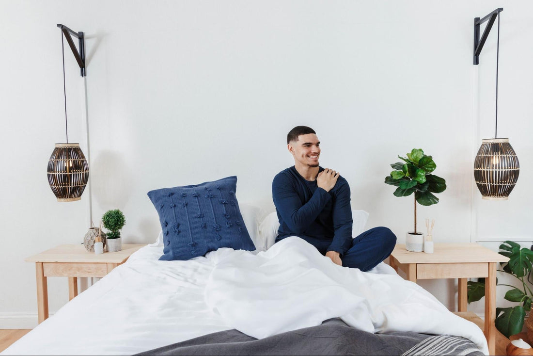 Relaxed man smiling on a bright, tidy bed with plants and hanging lanterns, calm morning bedroom scene for restful sleep